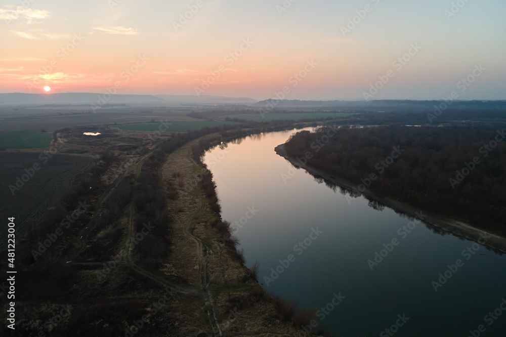 Aerial view of wide river flowing quietly in rural countryside in autumn evening