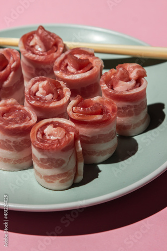 Bacon on a pink background. Raw bacon on a plate. Chinese sticks next to pieces of meat. Pig meat. rolled bacon