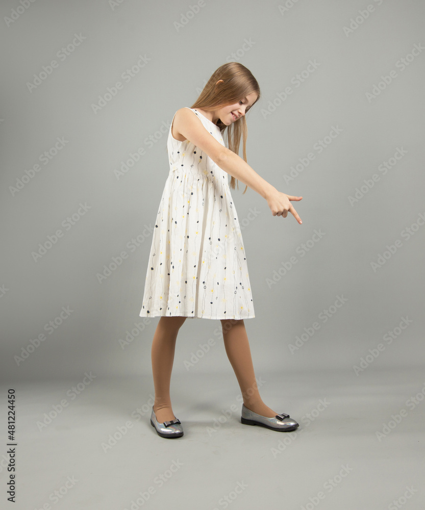 A beautiful girl smiles and points to the copy space. A young woman in a casual dress on a gray background A beautiful girl smiles and points to the copy space. A young woman in a casual dress on a gray background