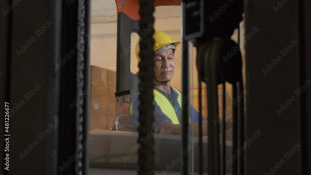 Asian old man working in warehouse and sitting on forklift moving boxes by forklift Asian old man working in warehouse and sitting on forklift moving boxes by forklift