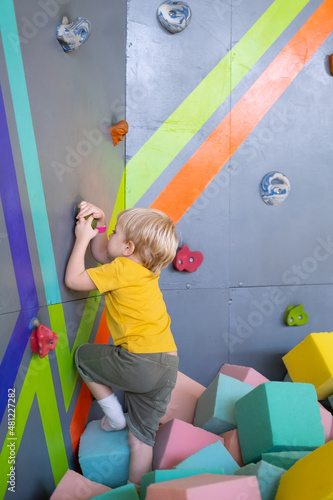 Little cute boy is climbing on vertical wall indoor in entertainment park