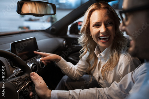 Young couple choosing a car in a car show room. Portrait of blonde hair woman with beautiful smile.