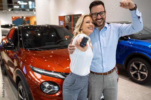 Happy couple standing in car salon with a key of their brand new car. Excited young married couple celebrate their good shopping. © GutesaMilos
