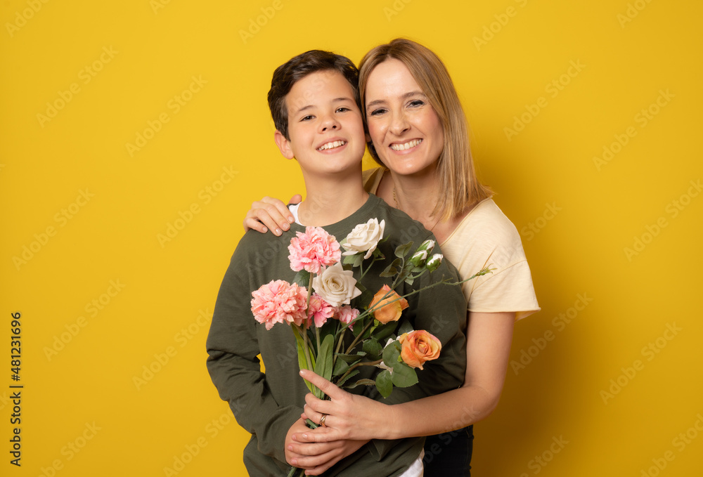 Smiling boy giving flowers to his mother isolated over yellow background. Smiling boy giving flowers to his mother isolated over yellow background.