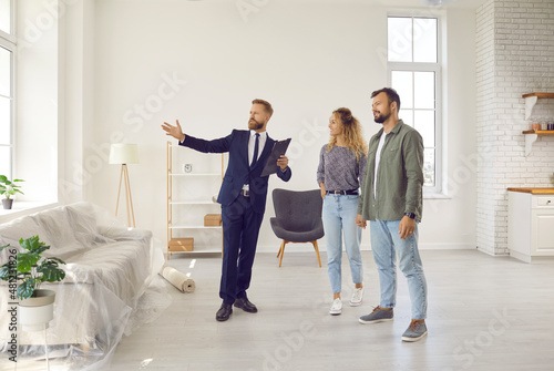 Realtor or real estate agent giving potential buyers or tenants tour about big house. Boyfriend and girlfriend or husband and wife who consider buying property looking at new modern spacious home photo