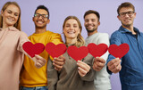 Studio group portrait of positive cheerful joyful kind mixed race multiethnic young people with happy faces holding red heart shaped Valentines and smiling. Close up. Love and Valentine's Day concept