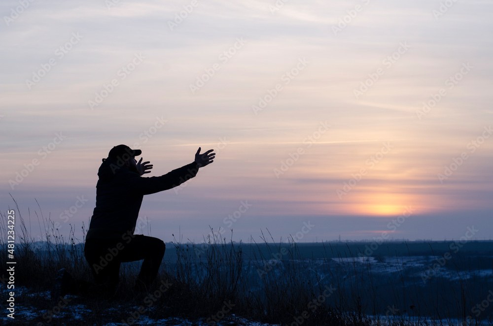 Fototapeta premium Prayer. Repentance. A man on his knees. Prayer. Silhouette of a man on a blue sky background. Kneeling Prayer to God. Glorification. Praising God. Christian. Zeal for God