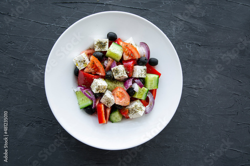 Fresh tasty greek salad on black stone concrete background, top view.