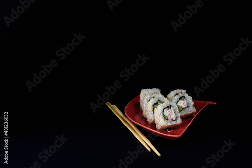 sushi rolls on a red saucer in the form of a fan on a black background of a chopstick