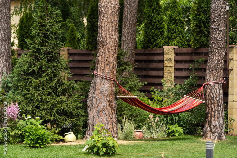 Red hammock swing in metal frame with nobody on green lawn in