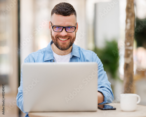 Happy young male businessman sitting in front of laptop outside working and having video conferencing online