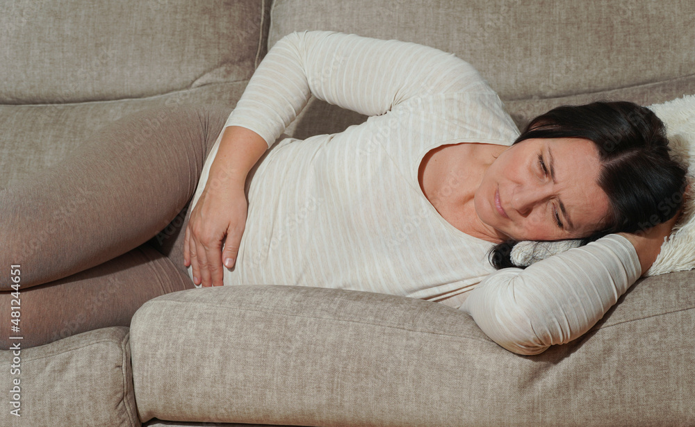 Middle aged mature woman suffering from stomach ache at home. Abdominal