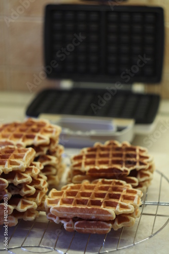 Freshly made homemade Viennese waffles on a mesh rack. Open waffle iron in the background.