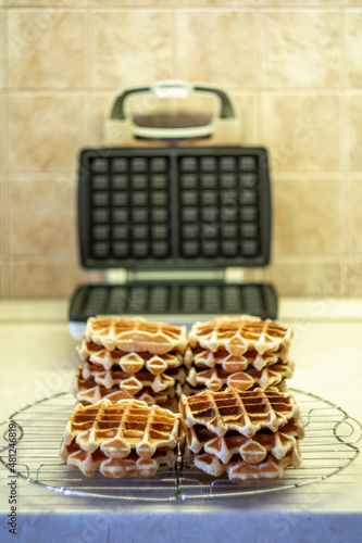 Freshly made homemade Viennese waffles on a mesh rack. Open waffle iron in the background.