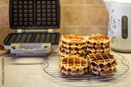 Freshly made homemade Viennese waffles on a mesh rack. Open waffle iron in the background.