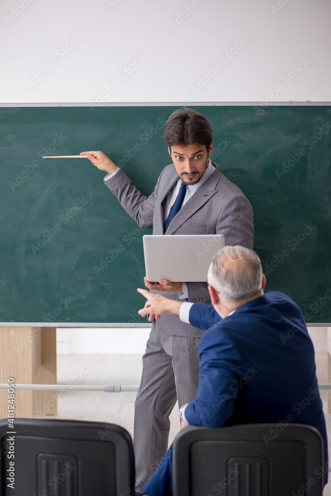 Young male employee and old boss in front of blackboard Young male employee and old boss in front of blackboard