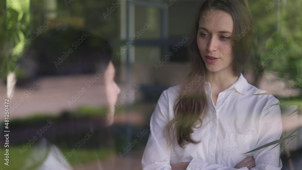 Shooting through glass of two female colleagues talking in slow motion discussing strategy idea indoors. Concentrated intelligent Caucasian women planning business in office. Slow motion Shooting through glass of two female colleagues talking in slow motion discussing strategy idea indoors. Concentrated intelligent Caucasian women planning business in office. Slow motion