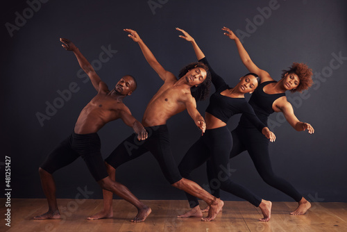 Perfectly synchronised. A group of dancers performing a dramatic pose in front of a dark background.