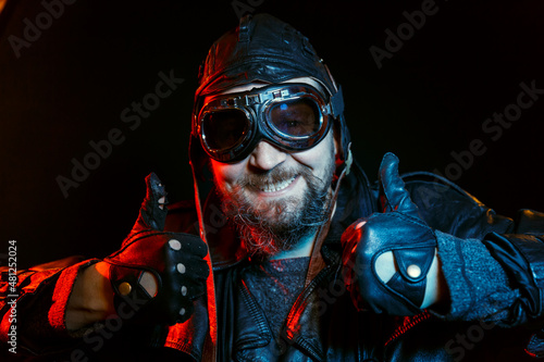 Portrait of retro driver with beard wearing vintage glasses and leather helmet on a black background.