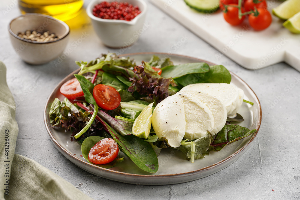 Salad with green leaves, lettuce, spinach, cherry tomatoes, mozzarella, olive oil, chilli pepper, lime juice on grey stone surface Salad with green leaves, lettuce, spinach, cherry tomatoes, mozzarella, olive oil, chilli pepper, lime juice on grey stone surface