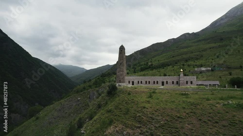 Caucasian battle tower, Ingushetia. Action. Aerial view of an ancient tower and a building on a green hill top surrounded by mountains. photo