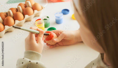 Little child decorates Easter eggs with colored food paint. Preparing for the feast of the holy Easter.