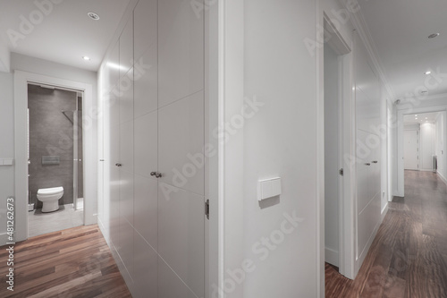 Long hallway with cabinet lined walls  corner cloakroom with open door and white built-ins with dark wood floor