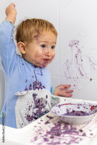 niño travieso desafiando en tirar la cuchara de su desayuno tras manchar toda la cocina con su comida
