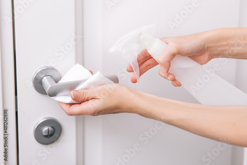 Cleaning white door handles with an antiseptic wet wipe and sanitizer spray. Disinfection in hospital and public spaces against corona virus. Woman hand using towel for cleaning home room door link