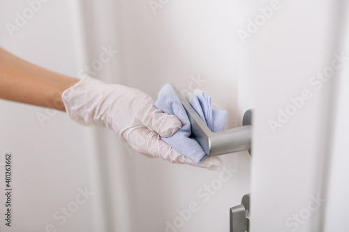 Cleaning door handle with blue wipe in white gloves. Woman hand using towel for cleaning home room door link. Sanitize surfaces prevention in hospital and public spaces against corona virus.