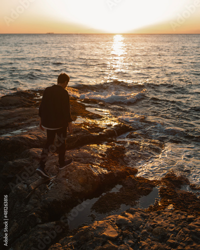 person walking on the rocks of the coast at the sunset.
