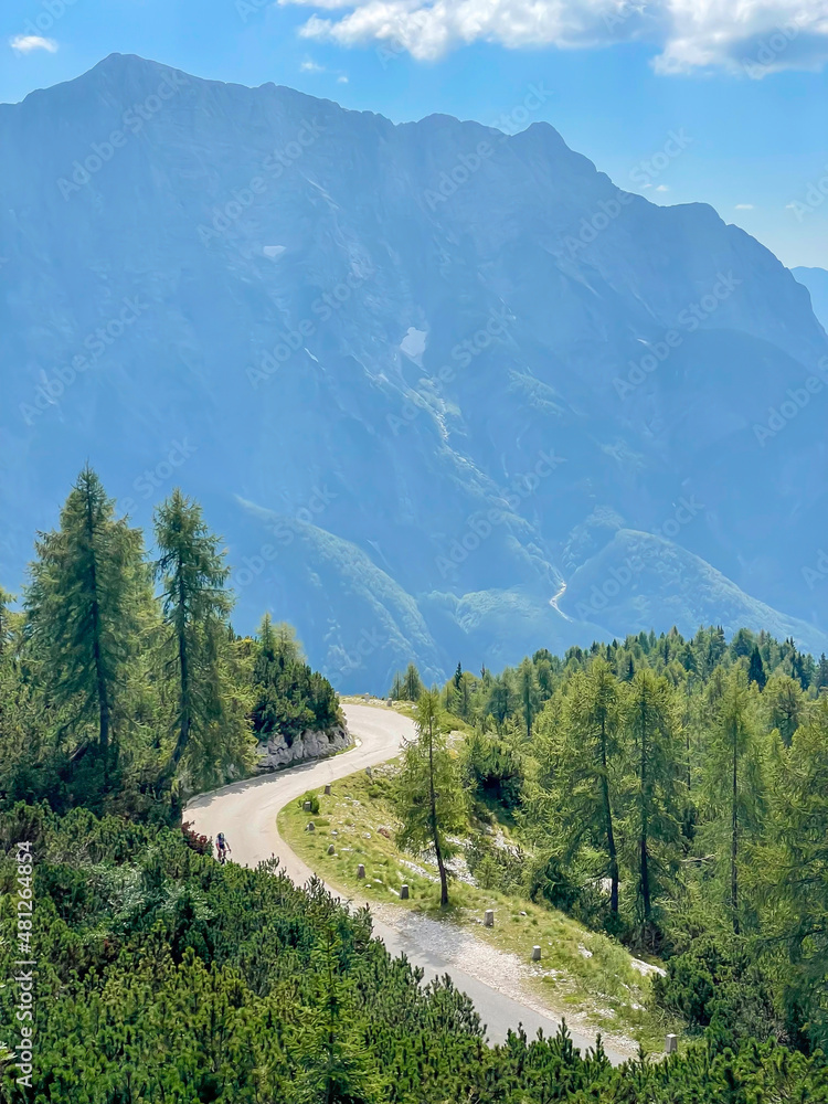 VERTICAL: Empty asphalt road winds along a mountain overlooking the Julian Alps.