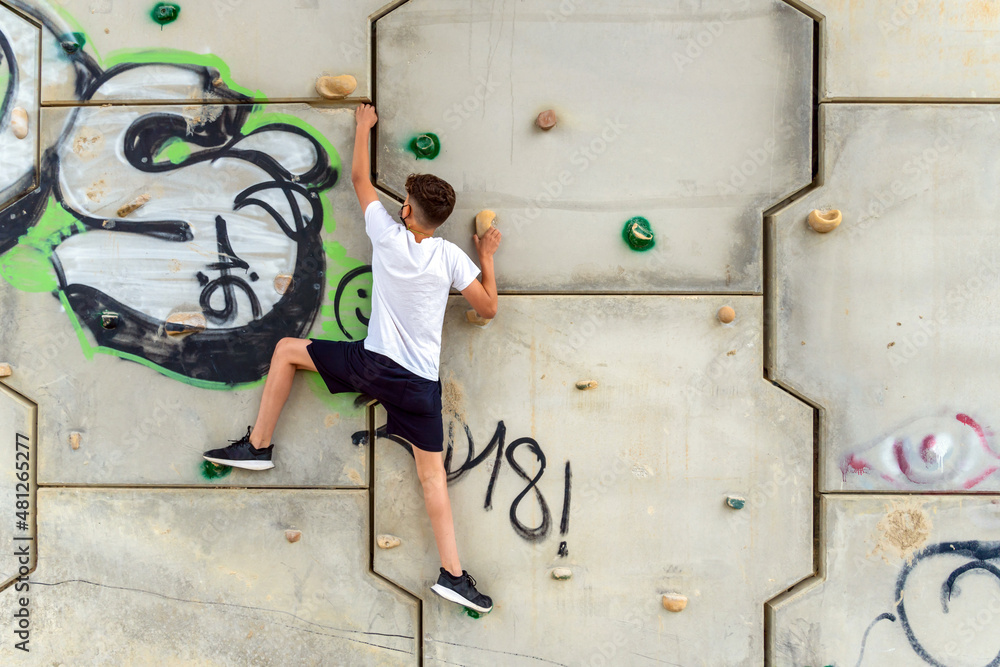 Young male using the hands to climbing up a wall with grips on it and a graffiti painted on the wall Young male using the hands to climbing up a wall with grips on it and a graffiti painted on the wall