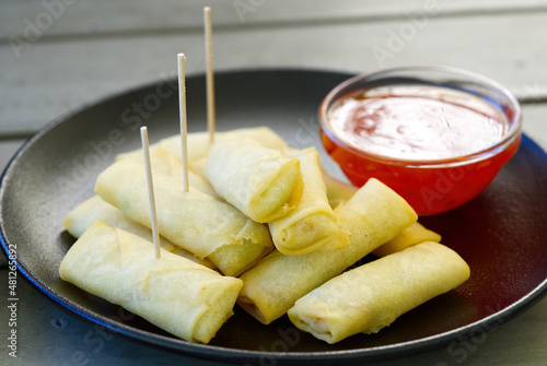 A plate of spring rolls with sweet chili dip sauce. outside restorante close up photo