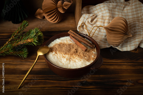 Scandinavian-style rice porridge. The rice pudding is in a blue ceramic bowl on a wooden table, with gingerbread cookies, cinnamon and dried orange slices.