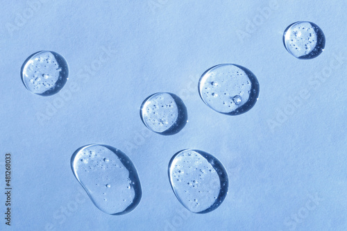 Cosmetic hydrating product or ingredient concept. Blue drops of transparent liquid on a light background. Drops gel or oil close up. Abstract backdrop.