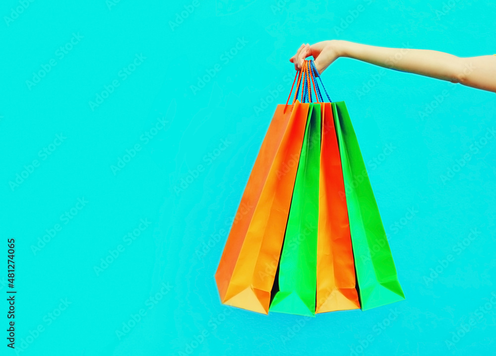 Female hand holding and showing colorful shopping bags on blue background