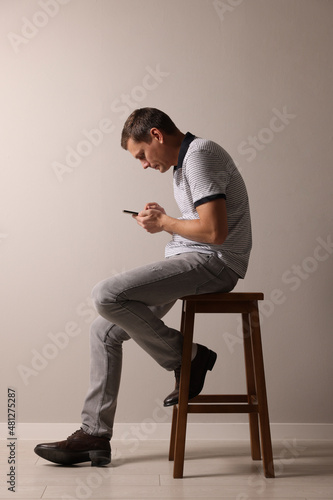 Man with bad posture using smartphone while sitting on stool against grey background