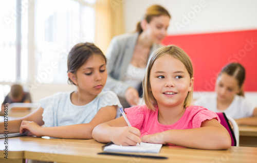 Portrait of two positive small school girls sitting together in classroom during lesson in elementary school