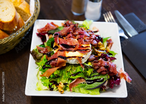 Portion of goat cheese salad with greens, jamon and balsamic sauce on dark wooden table