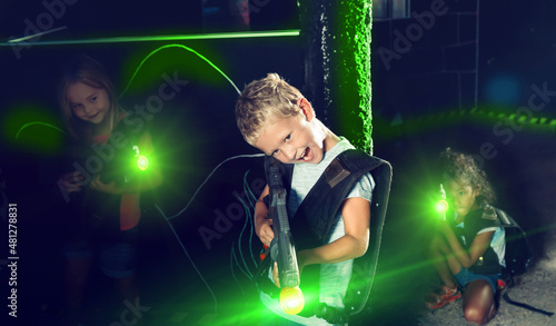 Emotional teen boy with laser pistol playing laser tag with friends on dark labyrinth. High quality photo