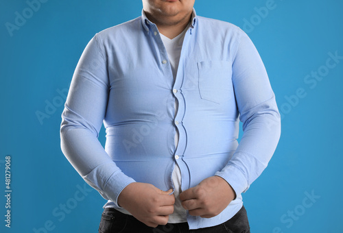 Overweight man trying to button up tight shirt on light blue background, closeup photo