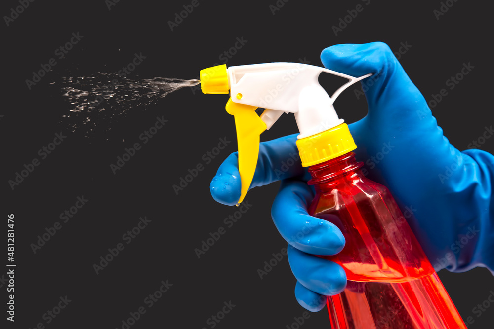 water sprayer bottle in a hand with gloves on a dark background with liquid spray. household items for home water sprayer bottle in a hand with gloves on a dark background with liquid spray. household items for home