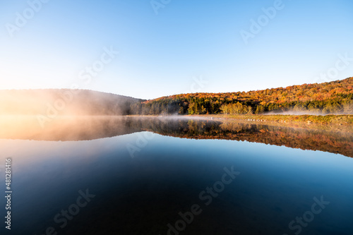 Spruce Knob lake blue water in West Virginia mountains fall autumn season and fog mist sunrise morning glowing yellow orange sunlight in Monongahela National Forest trees foliage