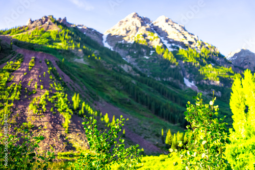 Maroon Bells rocky mountain peak view in Aspen, Colorado in July summer on trail path road view of green foliage on sunny day