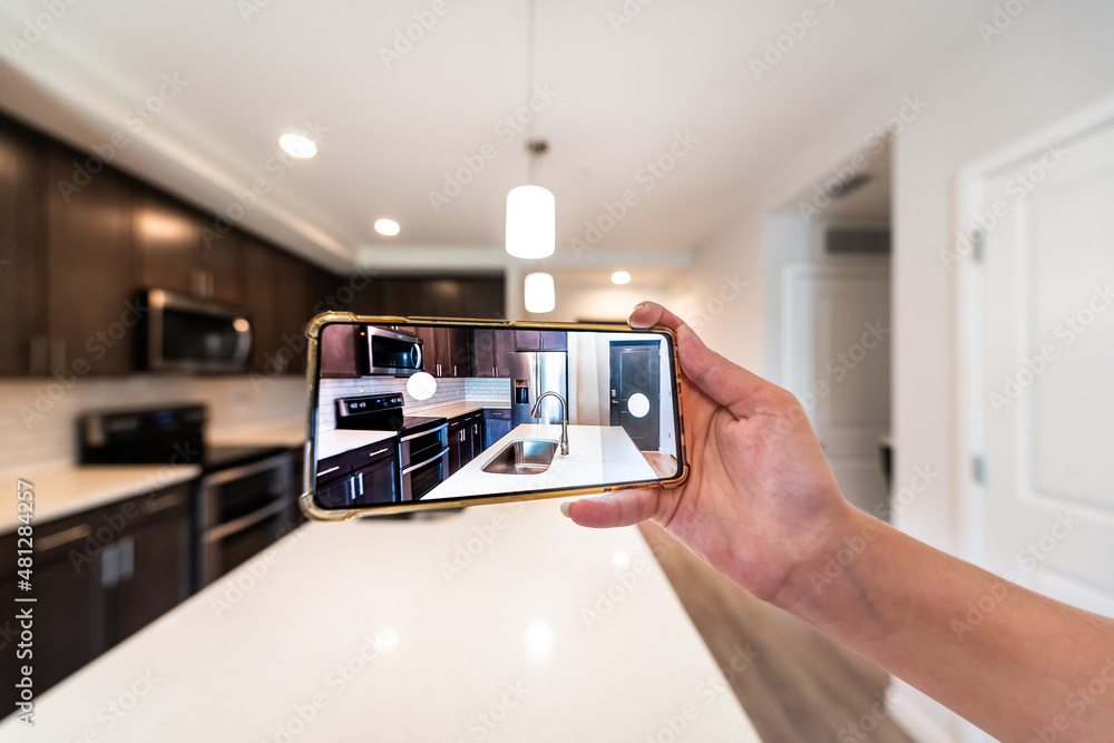 Hand photographing house apartment kitchen island room for sale or rent with phone smartphone closeup point of view in modern luxury condo home with blurry bokeh background - obrazy, fototapety, plakaty 
