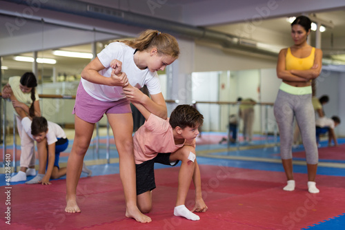 Positive teenager kids in pair exercising self-defense movements during group class