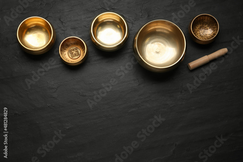 Golden singing bowls and mallet on black table, flat lay. Space for text