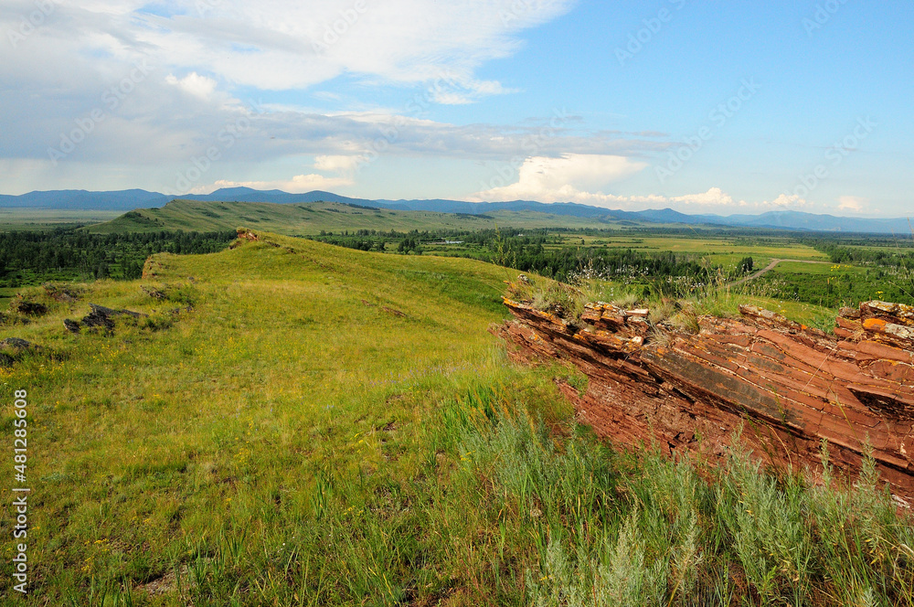 Layered stone formations on top of a hill overlooking the hilly steppe.
