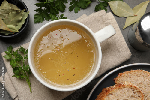 Hot delicious bouillon in cup on grey table, flat lay photo